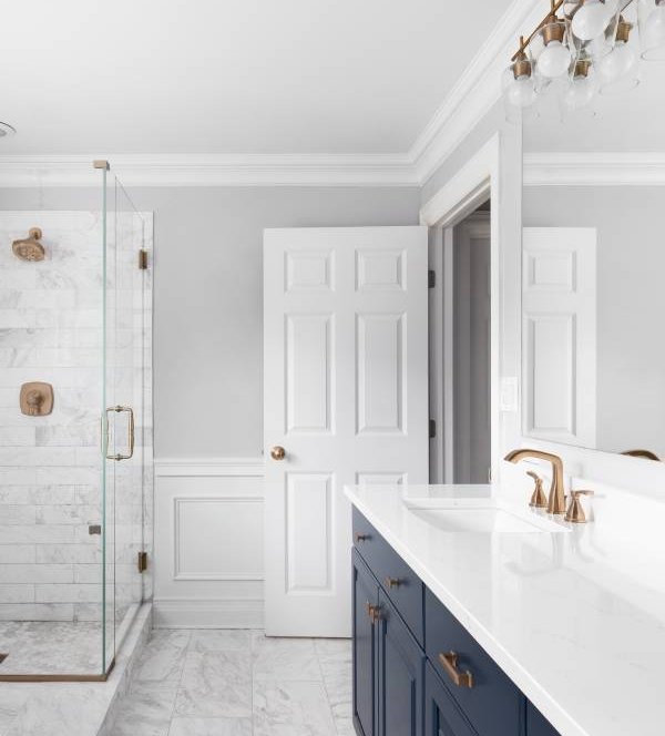 Newly renovated bathroom with a tiled floor, glass shower doors, gold accented light fixtures, and blue vanity marbled quartz counter tops.